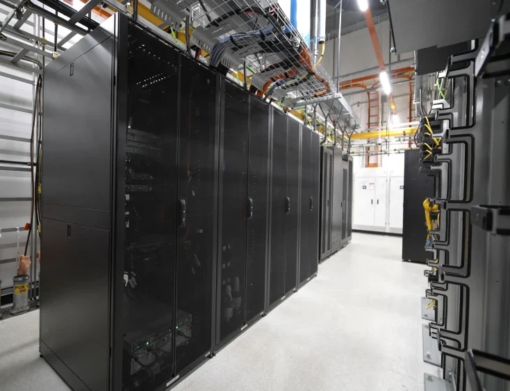 Server room with rows of black server racks and overhead cable management.